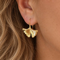 A close-up of a person's ear wearing a gold ginkgo leaf drop earring