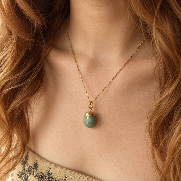 A close-up of a woman wearing a delicate gold chain necklace with a small oval green stone pendant.