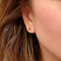 A close-up of a person's ear wearing a small gold leaf stud earring, with brown hair and skin visible.