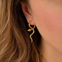 A close-up of a model's ear wearing a textured gold snake-shaped stud earring, with her hair and skin visible.