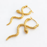 A pair of gold snake-shaped hoop earrings with textured scales and loop backs, displayed on a clean white background.