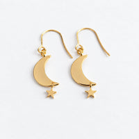 A pair of gold crescent moon and star drop earrings on a clean white background.