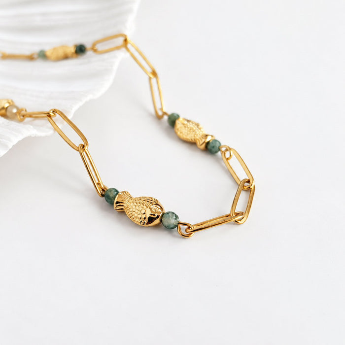 A gold link chain necklace featuring textured gold fish charms and small green faceted beads, displayed on a clean white surface.