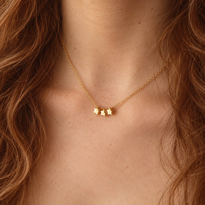 A delicate gold chain necklace worn by a model, featuring three small star charms in the centre.